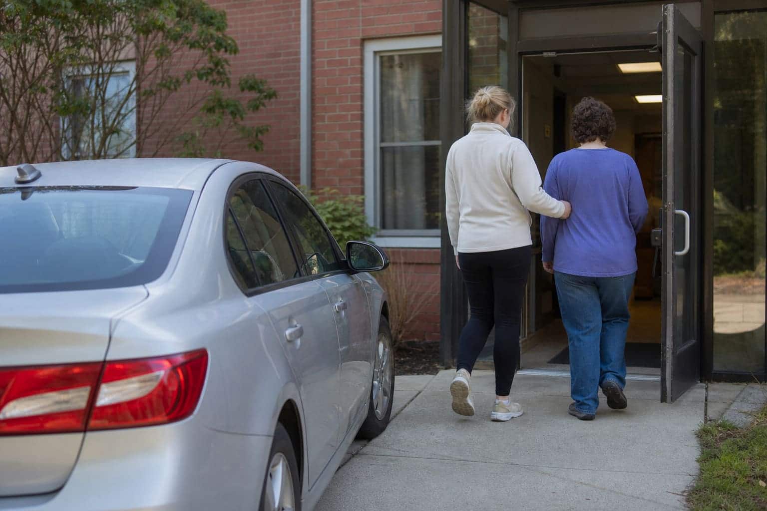 AI-generated scene: White female monitor escorting an ambulatory young adult into a day program